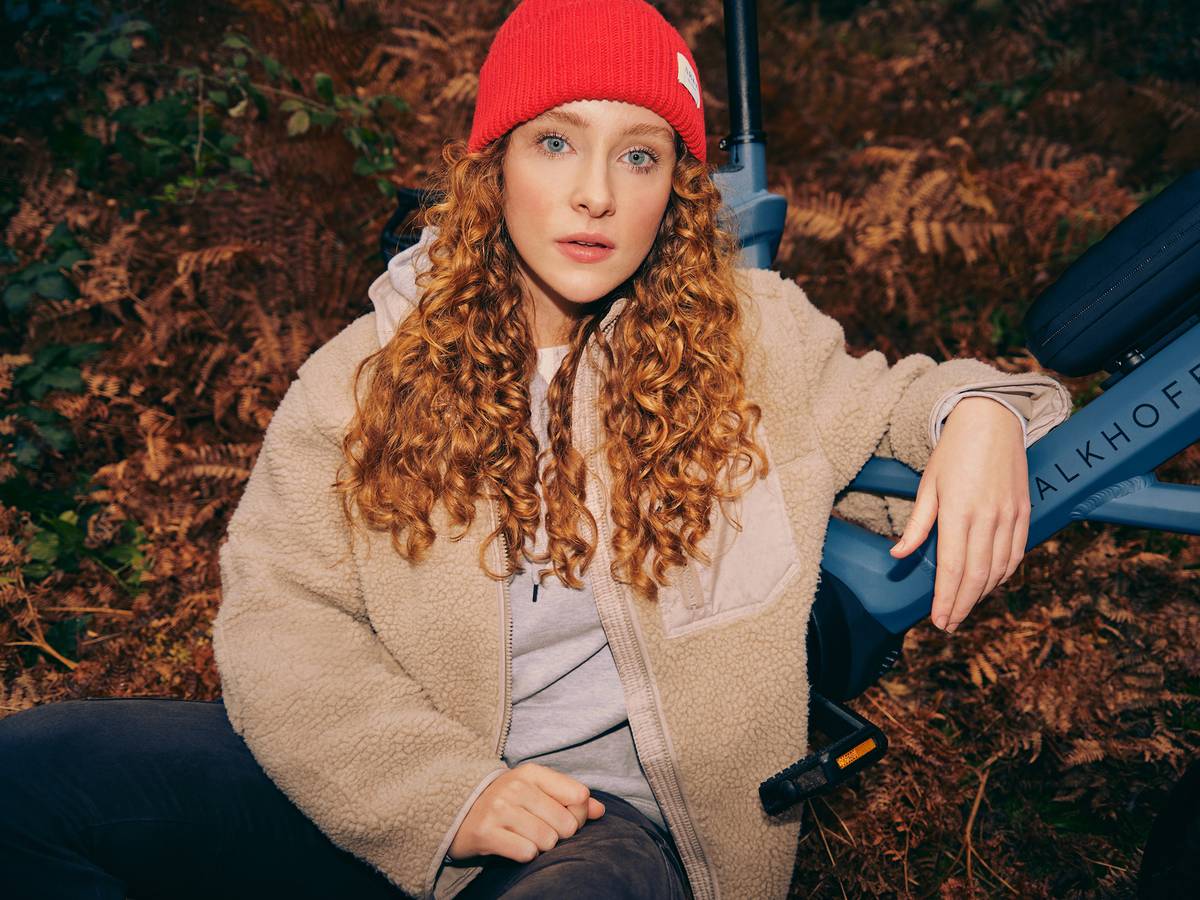 Woman with red hat is sitting in autumn leaves in front of bikes