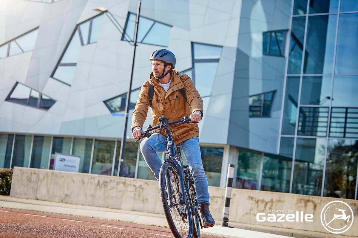 Man with helmet on Gazelle company bike in front of modern building