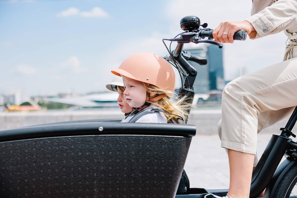 woman riding cargo bike with two kids in summer weather