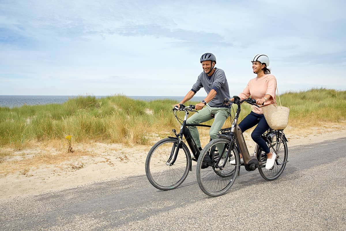 Couple rides Gazelle company bikes on bike path in dunes