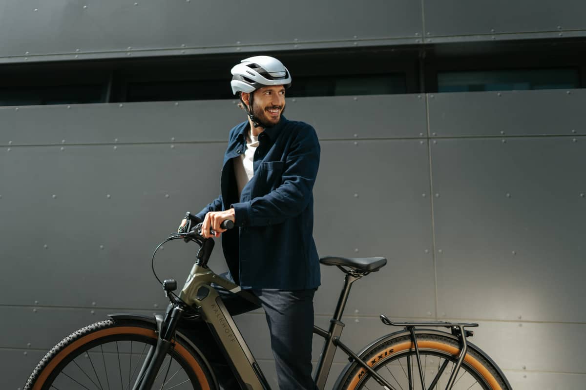 Man on e bike is standing with bike in front of wall, smiling and looking back