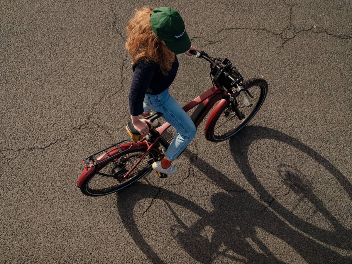 Frau mit Mütze auf rotem Rad auf Asphalt schaut auf Boden