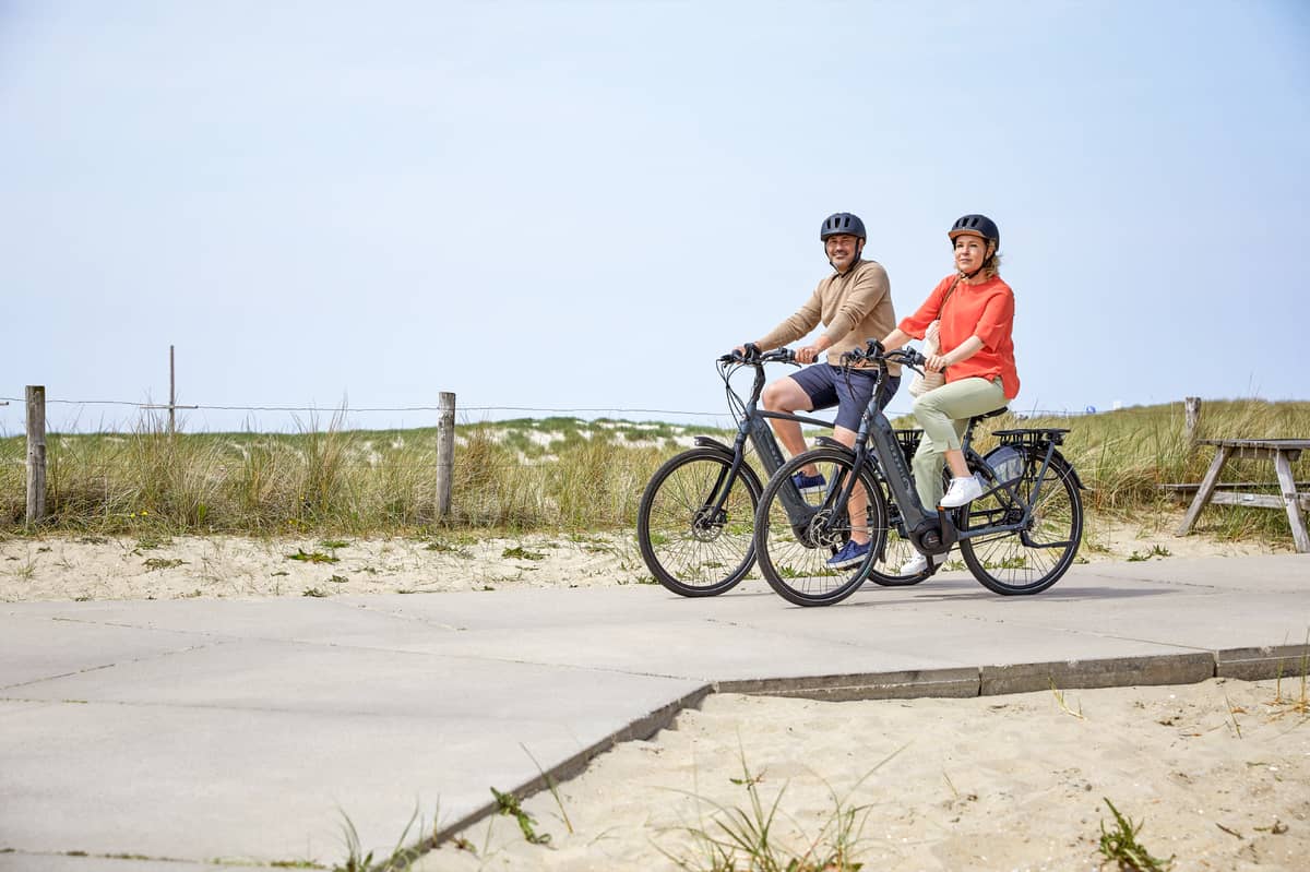 Couple on bikes on wooden path and dunes in background