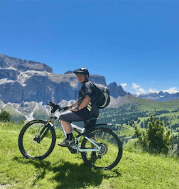 man with helmet and backpack sitting on bike in front of mountain panorama