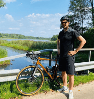 Mann steht neben Rennrad auf Brücke vor Fluss