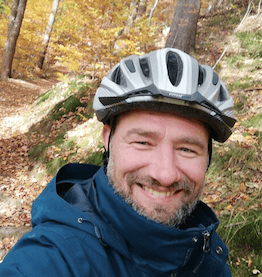 man with helmet in forest smiling towards camera company bike