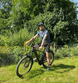 man on company bike smiling towards camera in front of green landscape