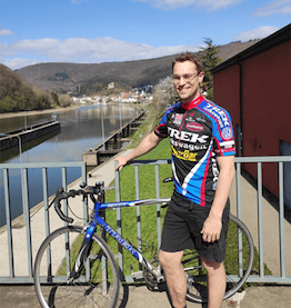 Mann mit Rennrad Dienstrad steht lachend auf Brücke