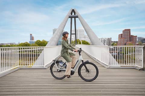 Frau mit Helm auf Gazelle E-Bike auf Brücke vor Stadt