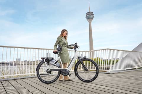 Frau steht neben Fahrrad auf Brücke vor Düsseldorf Skyline