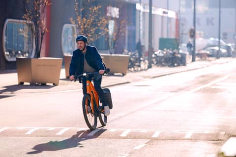 Mann mit helm auf Dienstrad fährt mitten auf Straße in Stadt