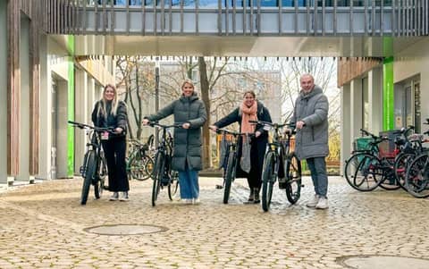 Vier Personen mit Fahrrädern stehen nebeneinander und lachen in Kamera