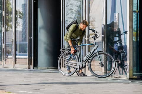 Mann mit Rucksack schließt Fahrrad vor Gebäude ab