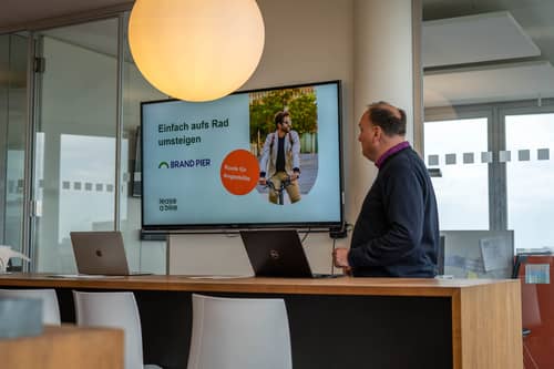 Man standing behind table and next to tv to present about bike leasing