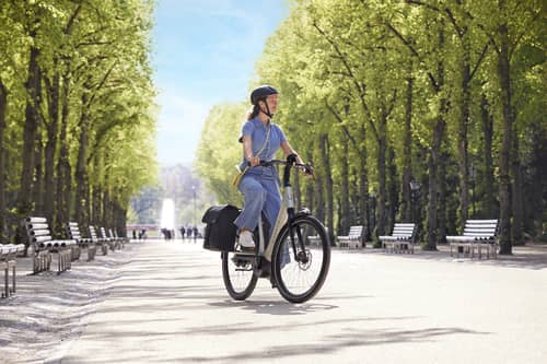 woman with Gazelle e bike rides through alley with trees on both sides