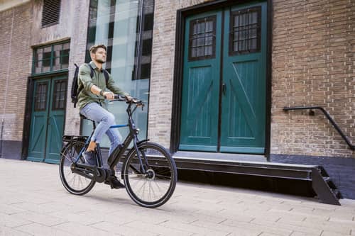 Man with backpack riding bike building in background