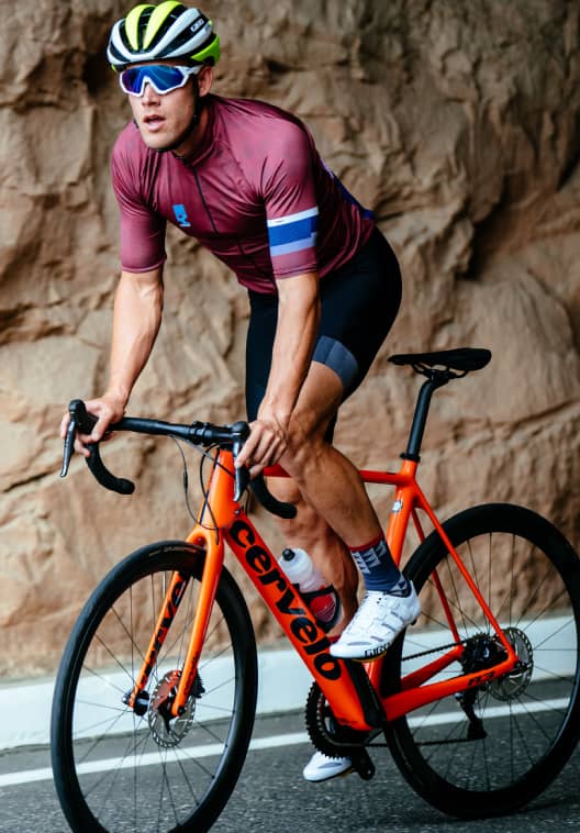 Man on orange road bike riding on street next to rock face