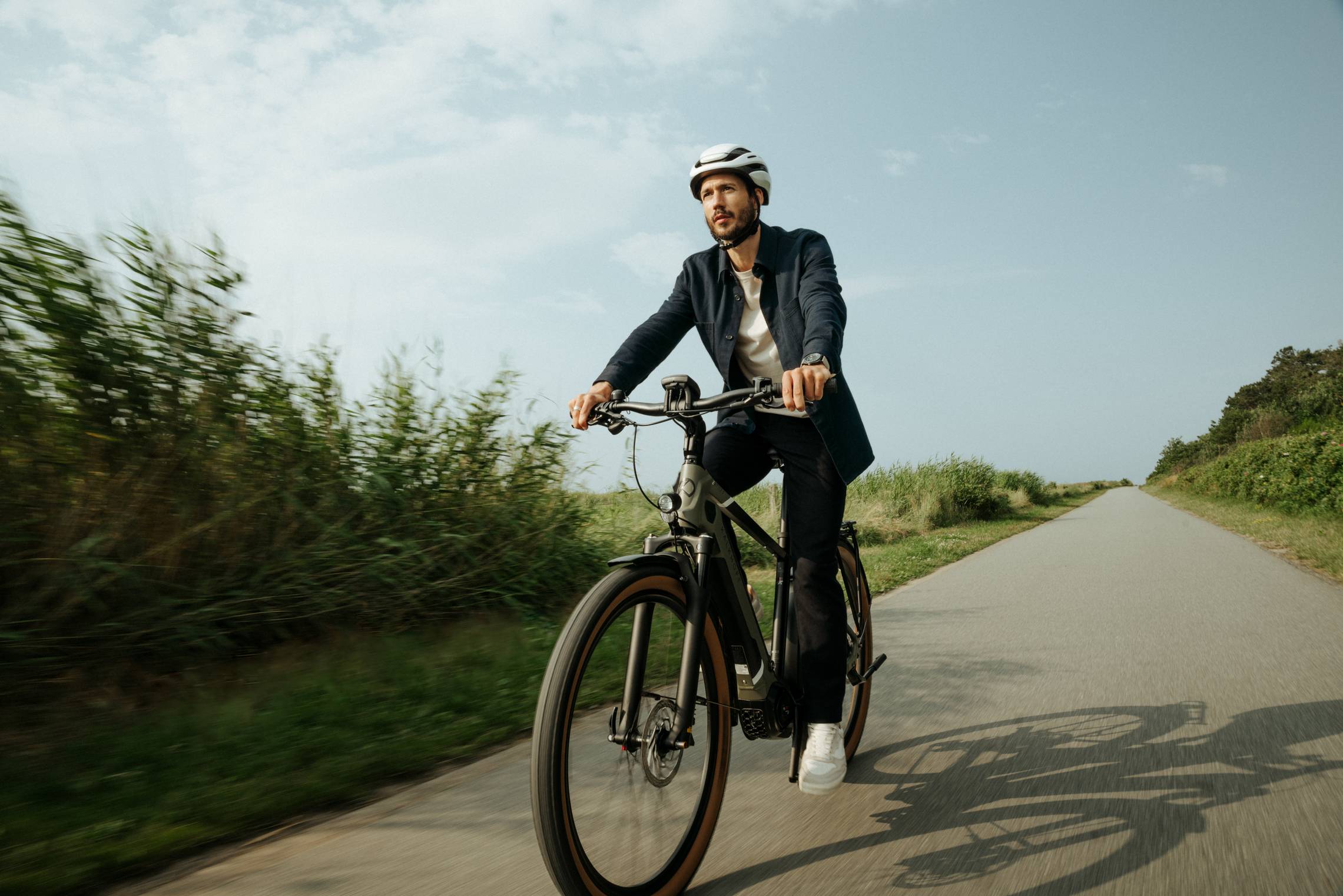 Mann mit Helm fährt auf Dienstrad auf Radweg in ländlicher Umgebung