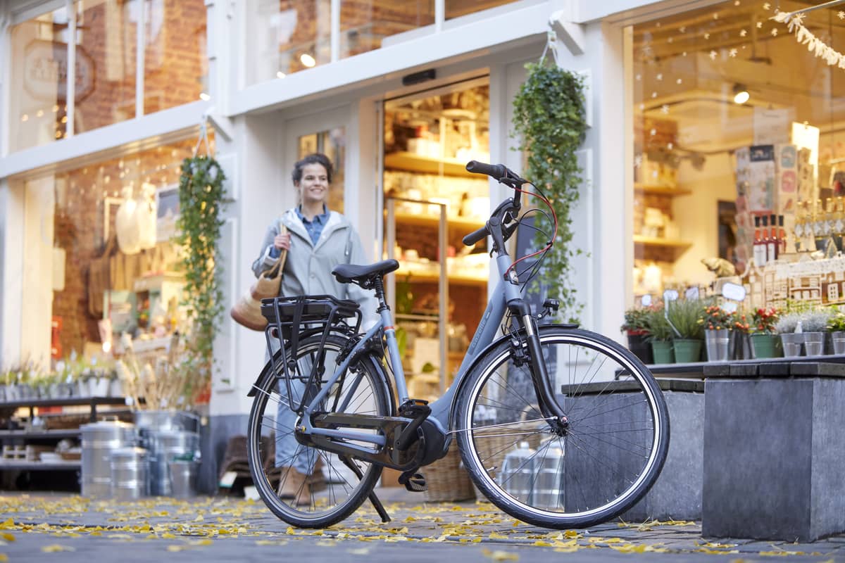 woman standing behind parking Gazelle bike with shop in background