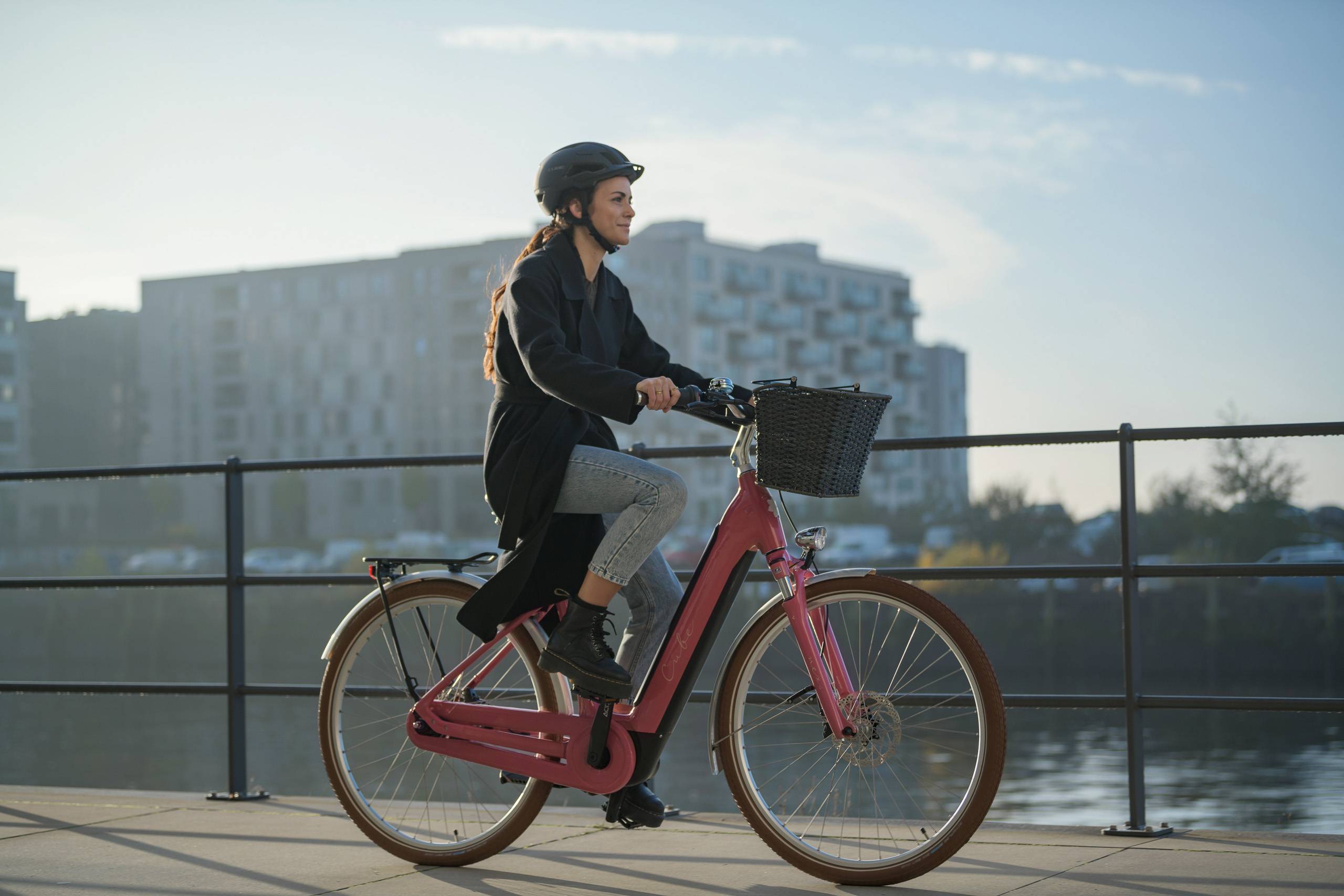 woman with helmet on cube bike in urban surrounding on bridge in front of river