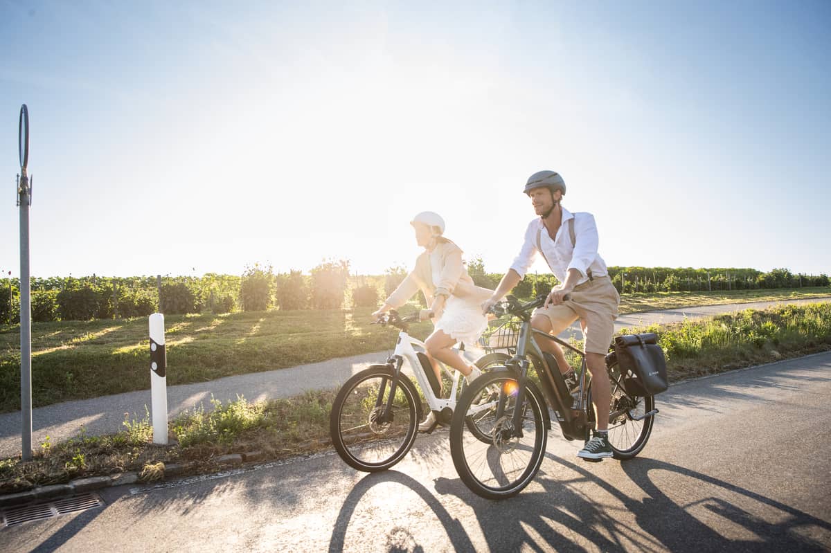 Couple on bikes on bike path next to street in sun