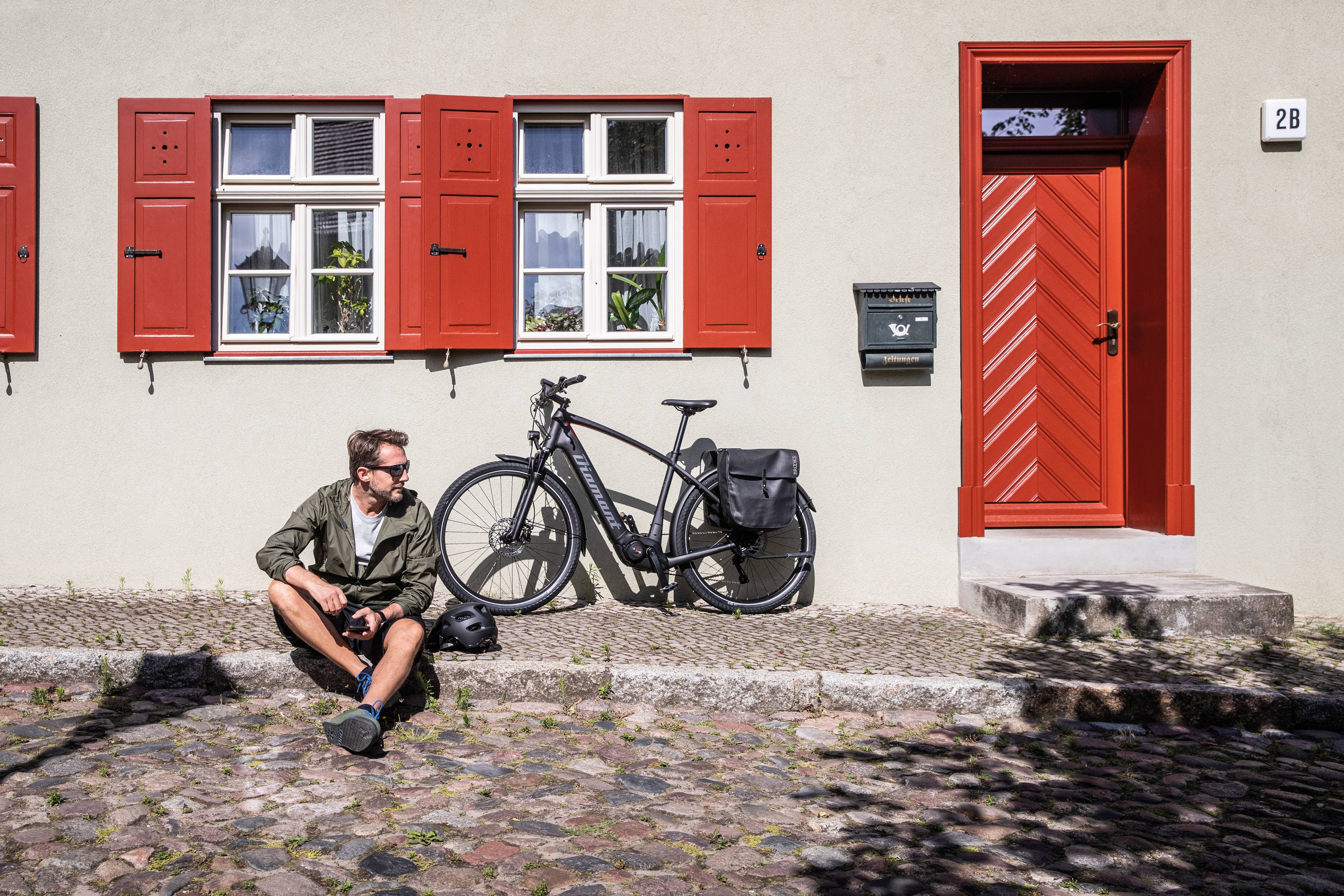 Mann sitzt auf Bordstein Fahrrad parkt dahinter an Hauswand