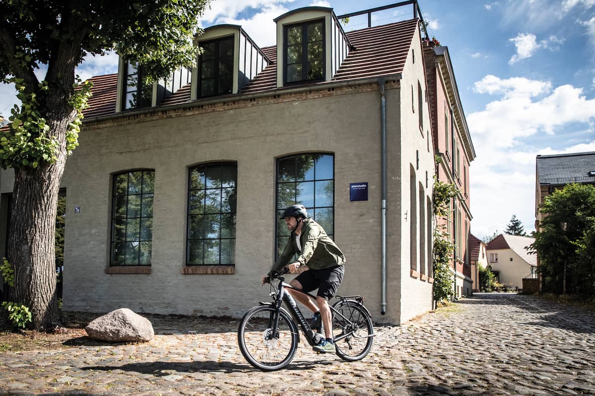 Radfahrer fährt mit Fahrrad auf Kopfsteinpflaster entlang von Wohnhaus