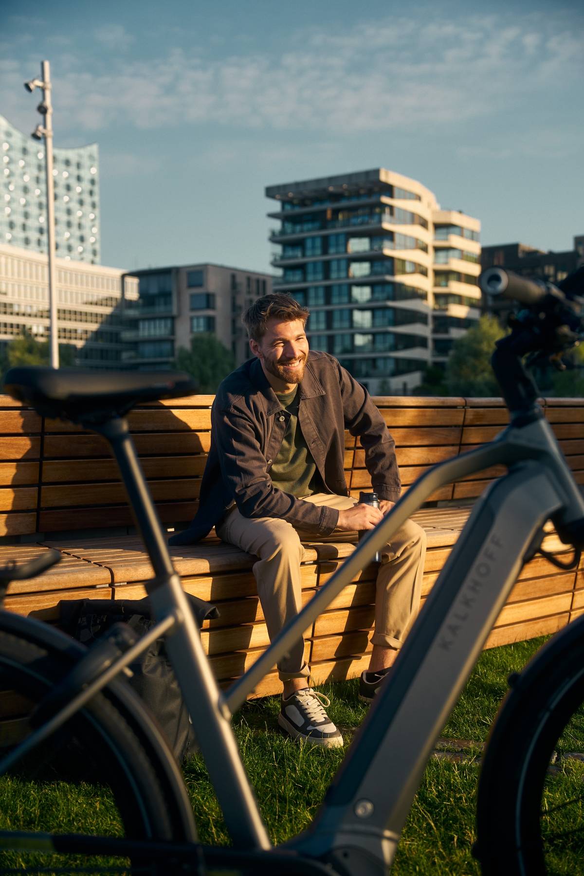 Man sitting on bench smiling, Kalkhoff bike in front of him