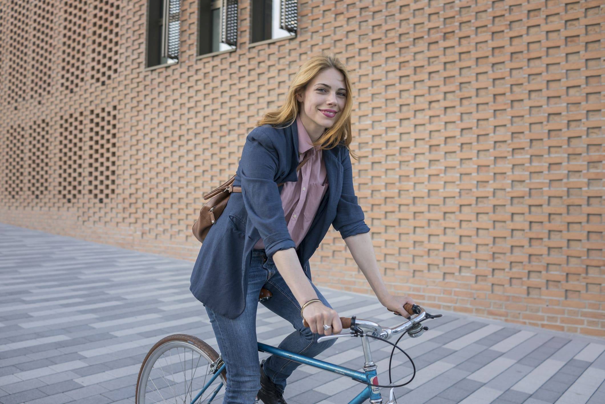 Junge Frau mit Rucksack vor Gebäude sitzt auf Fahrrad und lächelt