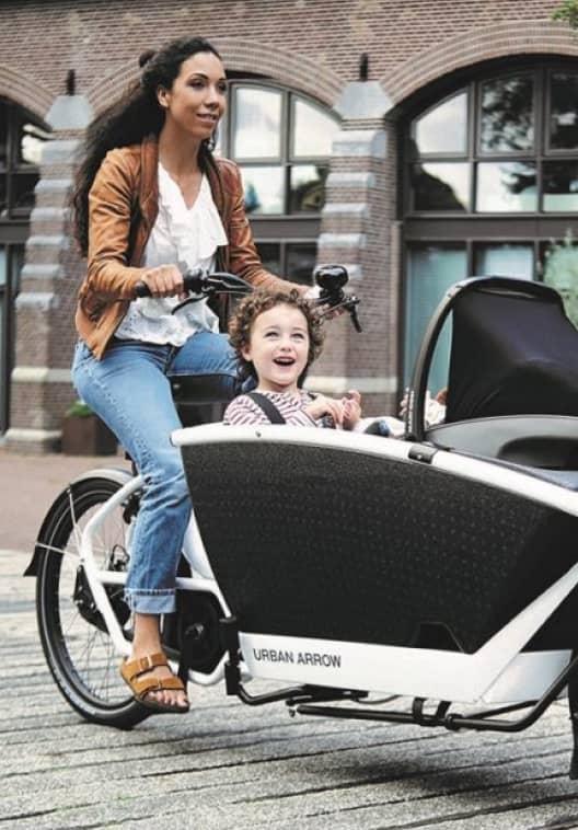 Woman on cargo bike with two kids in urban surrounding